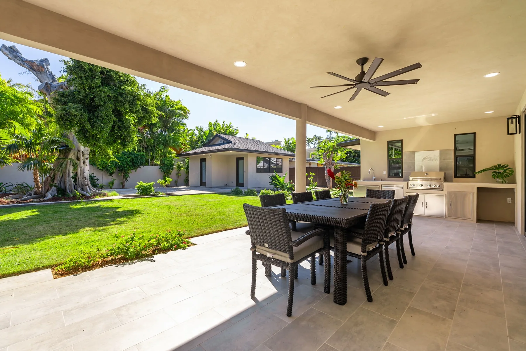 A covered outdoor dining area overlooks a green lawn and landscaped yard.