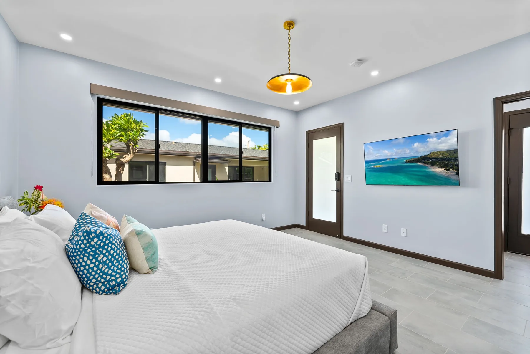 A bright bedroom with a large bed, a wide window, and a framed beach scene.