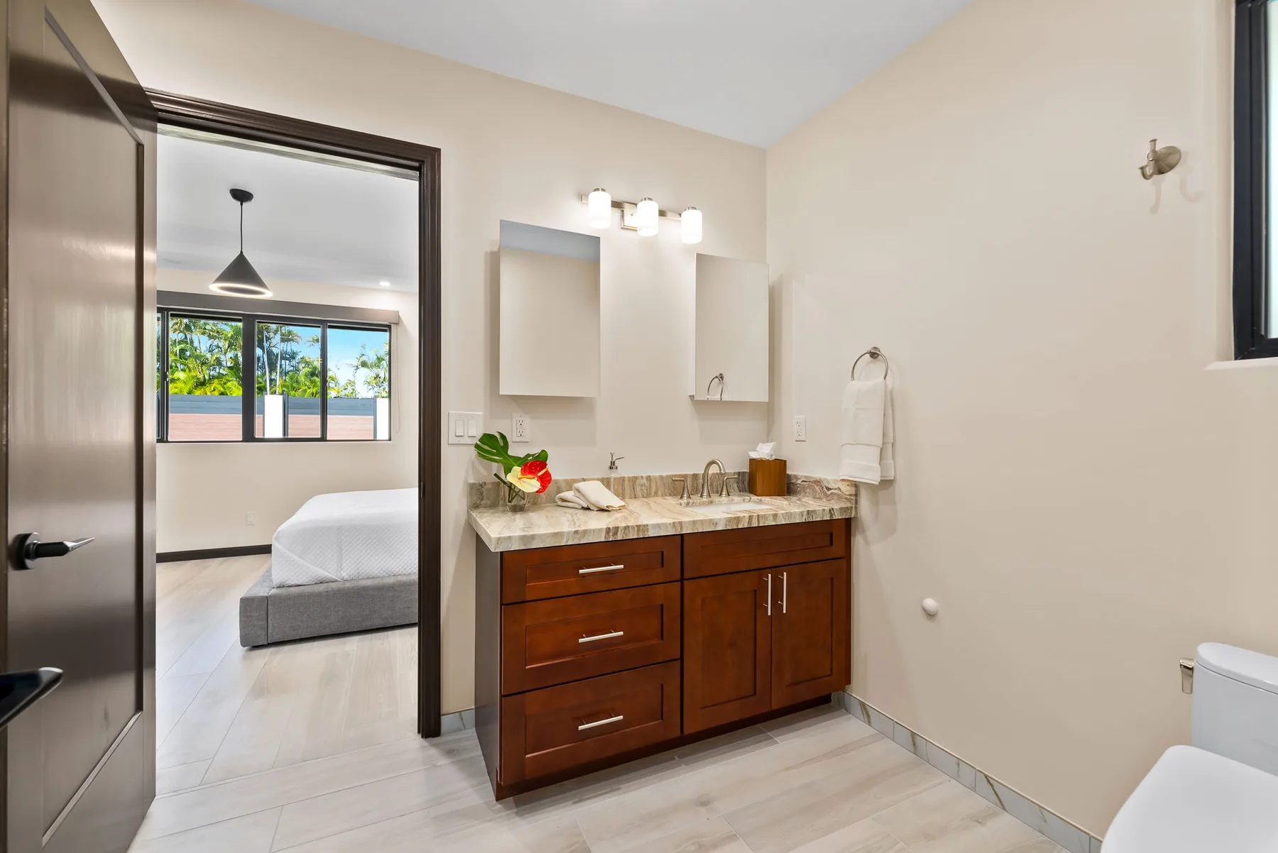 A bathroom vanity with a wide mirror and an open doorway to a bedroom.