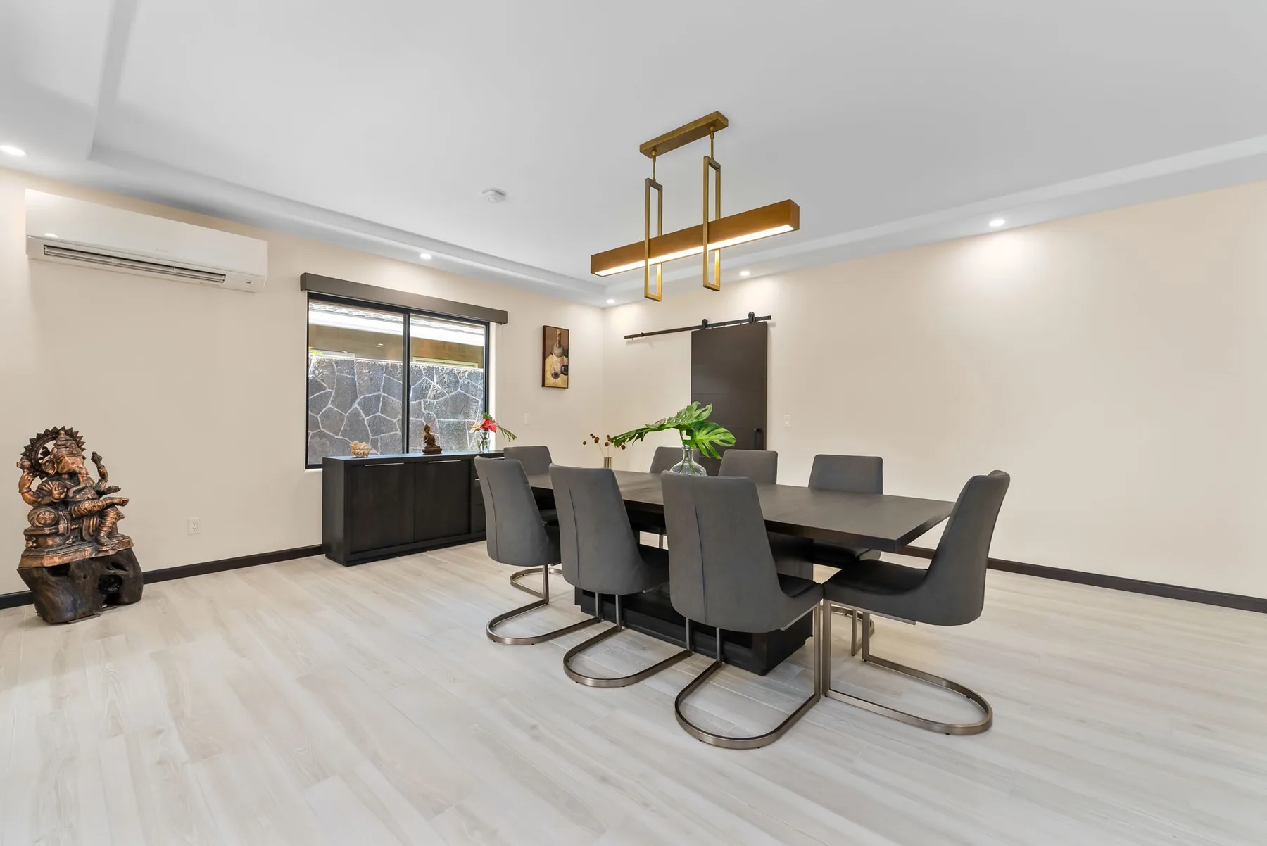 A modern dining room with a dark table, upholstered seating, and a gold ceiling light.