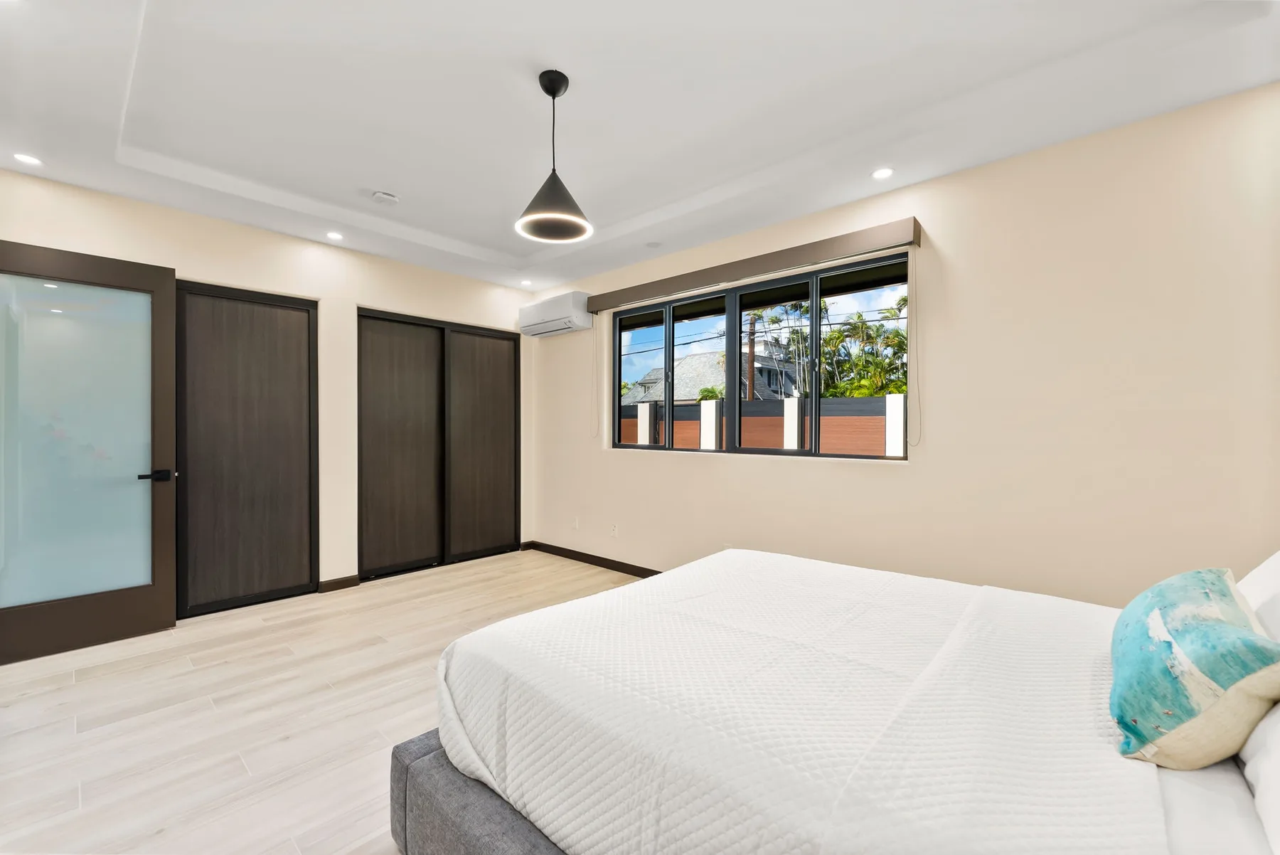 A bright bedroom with a bed, dark doors, and a window.
