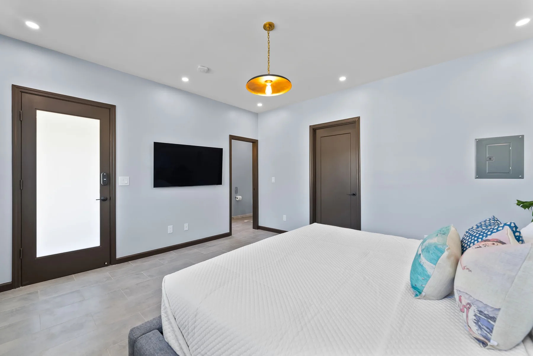 A bedroom with a bed, wall-mounted television, and dark-trimmed doors.