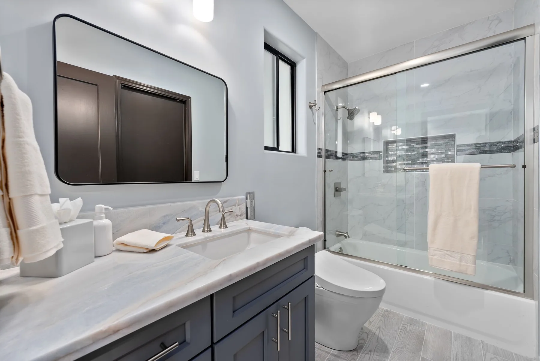 A bright bathroom with a vanity, mirror, toilet, and glass shower.