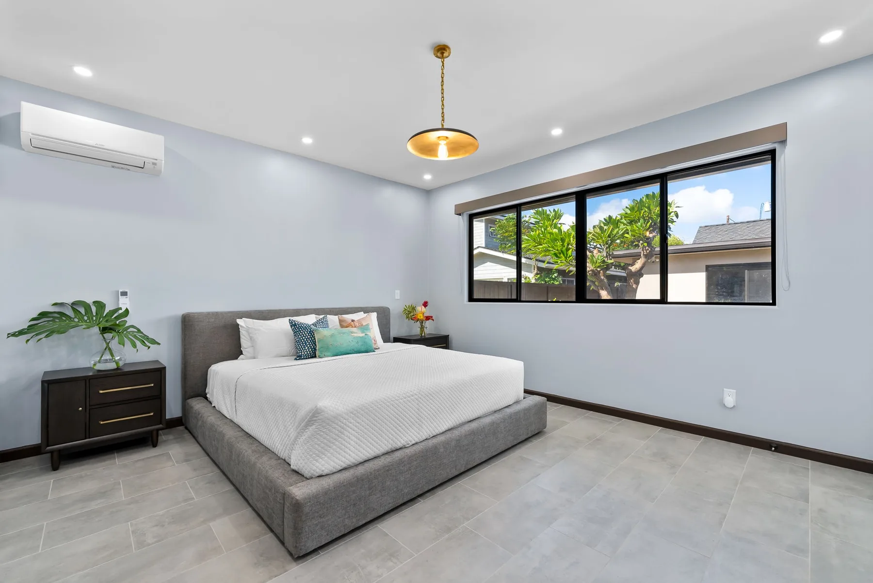 A bedroom with a bed beside a wide window overlooking greenery.