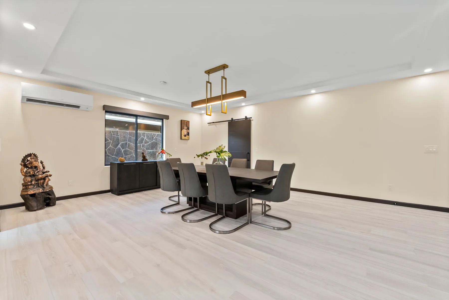A dining area with a long table and dark seating beneath a pendant light.