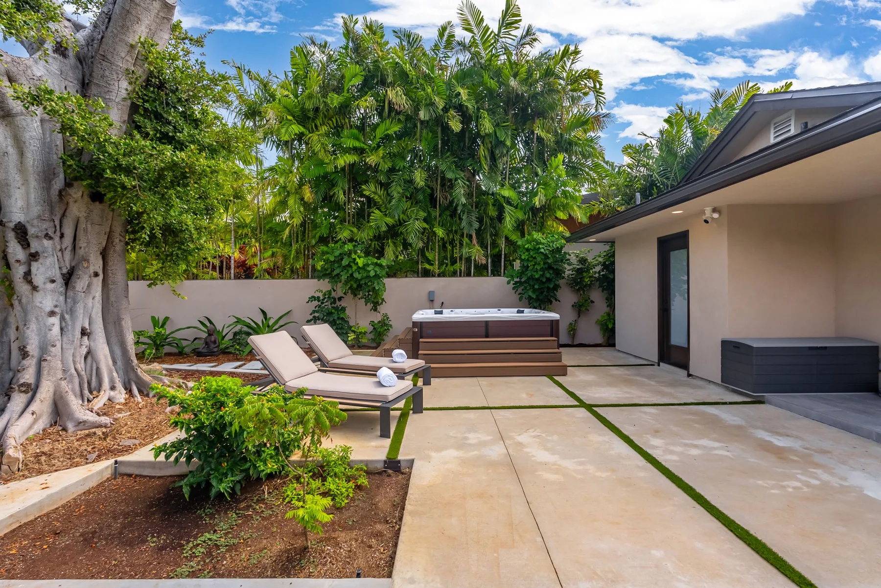 An outdoor patio with lounge seating, a hot tub, and tropical greenery.