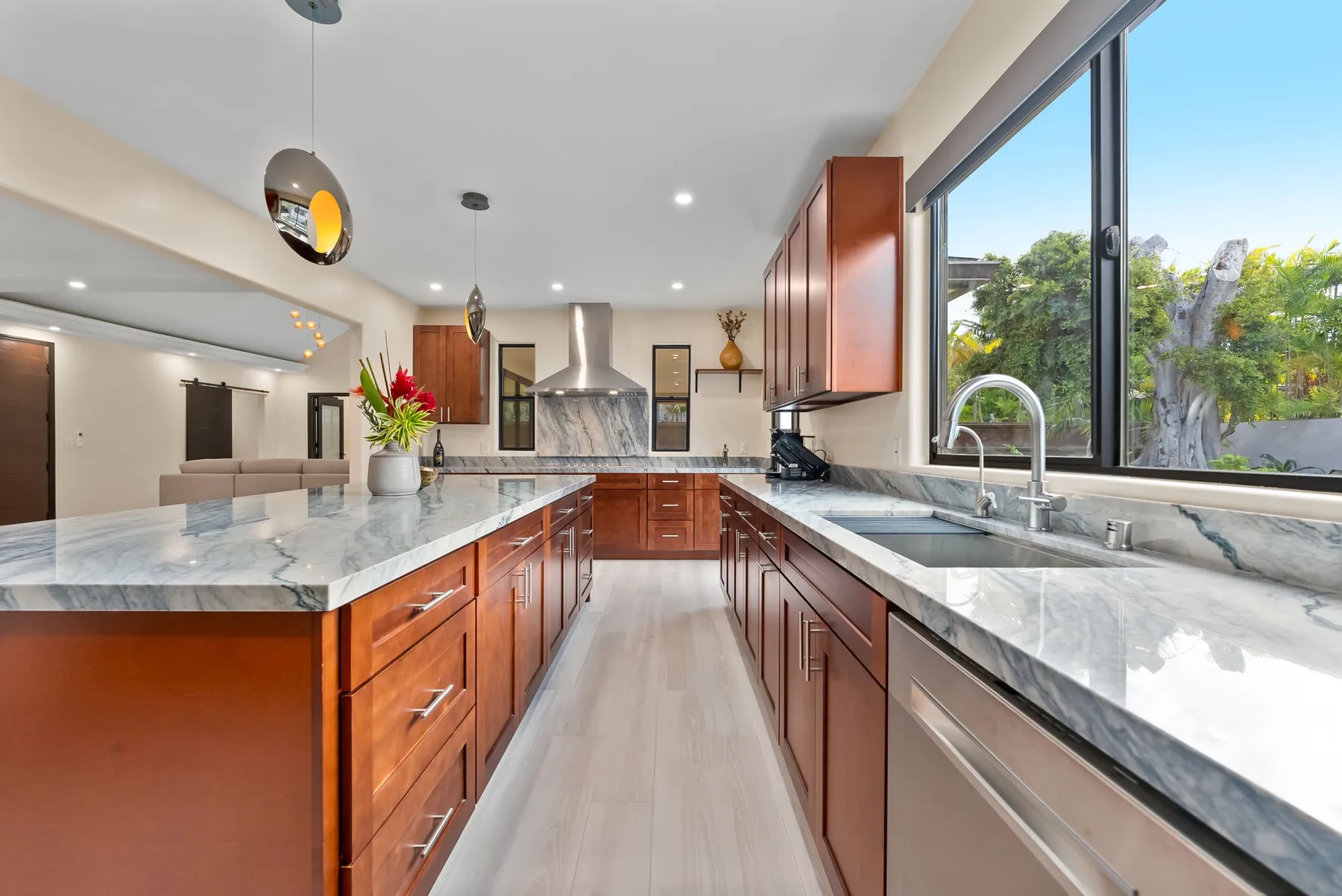 A modern kitchen with wood cabinetry, stone counters, and a large window.