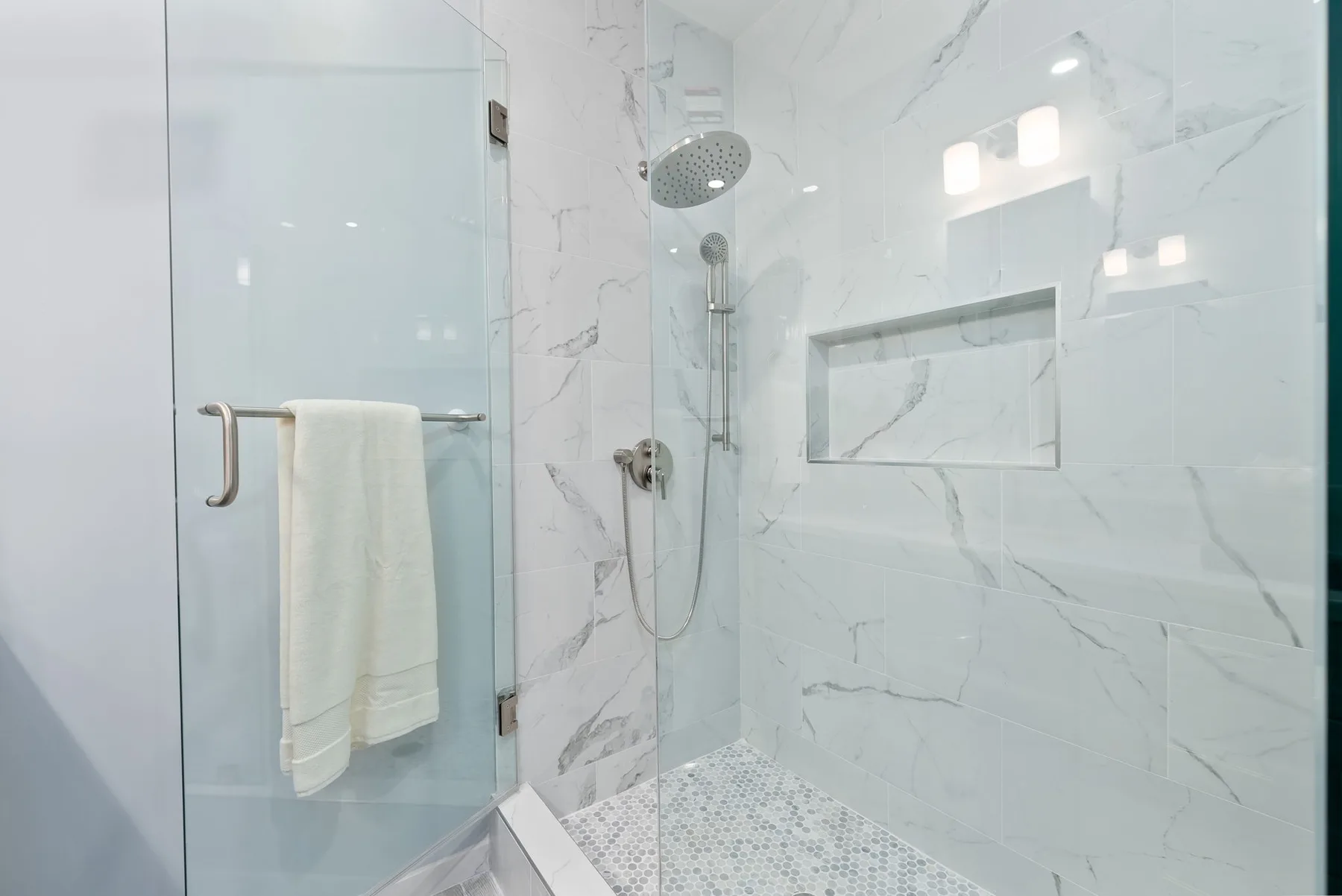 A bright tiled shower with a handheld showerhead and recessed wall niche.