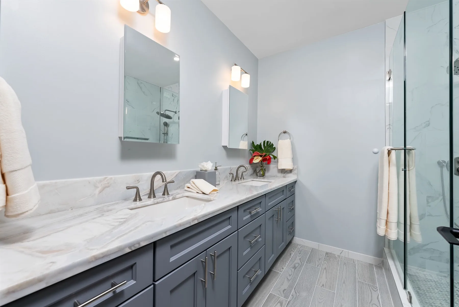 A bright bathroom features a long vanity with sinks and a glass shower.