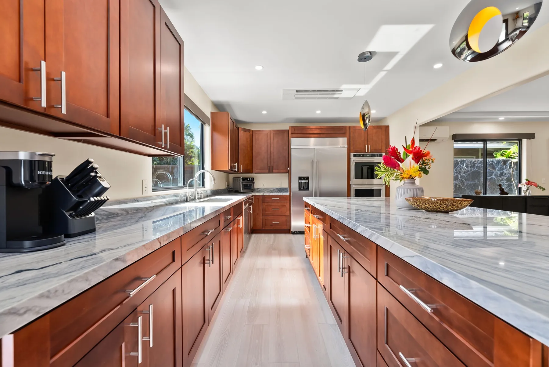 A modern kitchen with wood cabinets, stone counters, and stainless steel appliances.