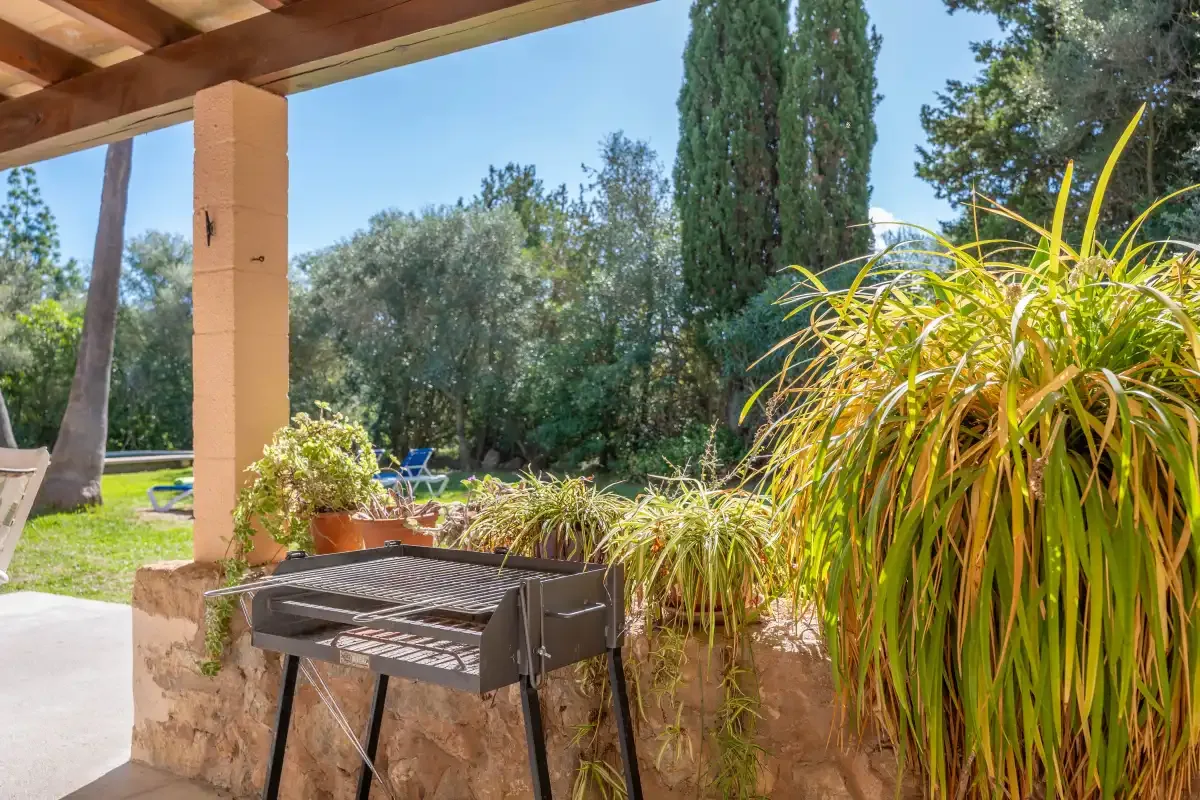 A covered outdoor patio overlooks a garden, with a barbecue beside the seating area.