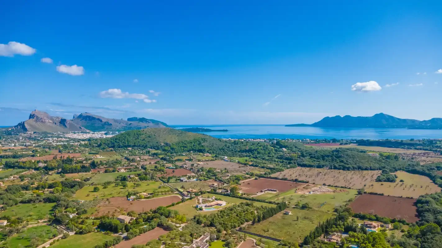 Aerial view of a coastal landscape with fields, hills, and distant mountains.