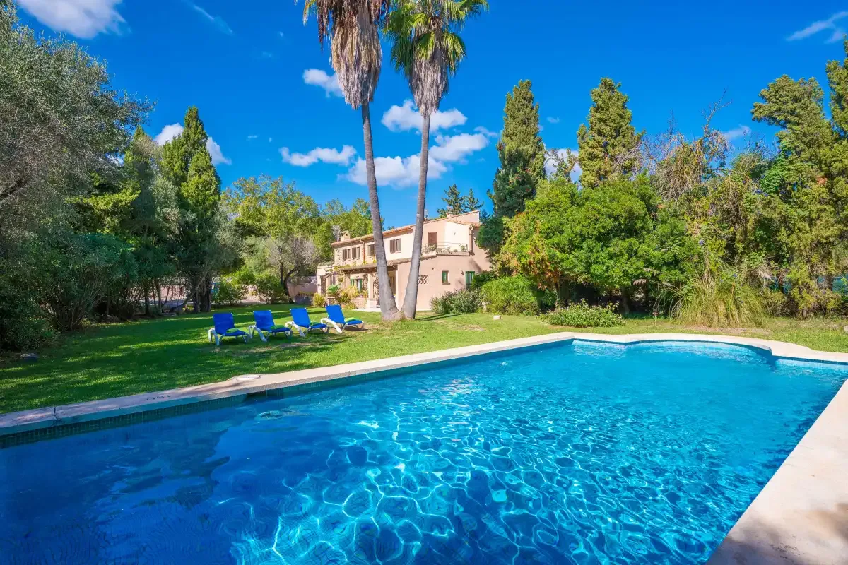 An outdoor swimming pool beside a green lawn, trees, and a house.