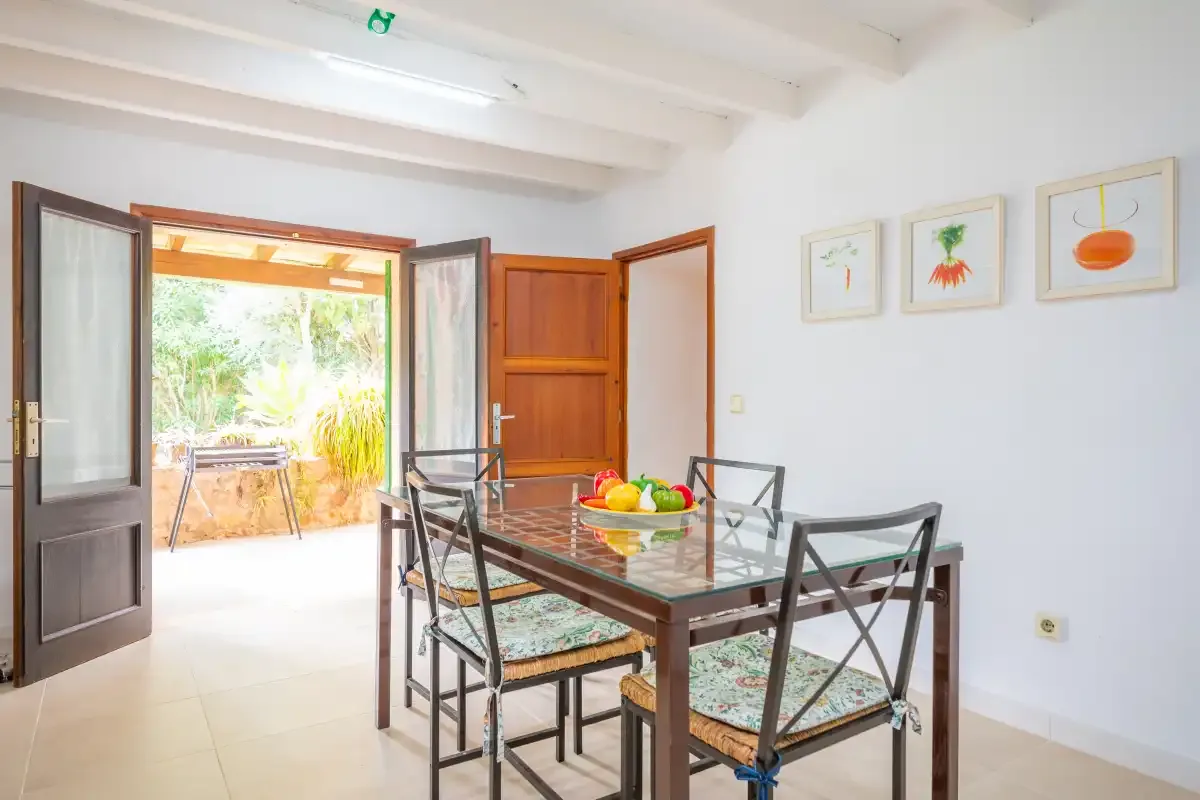 A dining area with a glass table and chairs beside open doors to a patio.