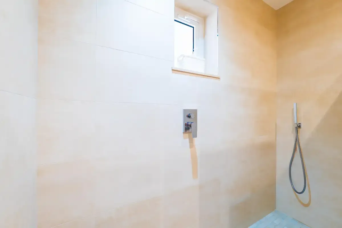 A tiled shower area with a small window and wall-mounted shower fixture.