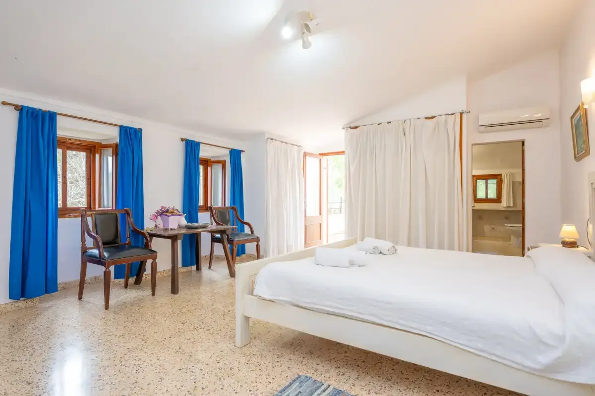 A bright bedroom with a large bed and seating beside the windows.
