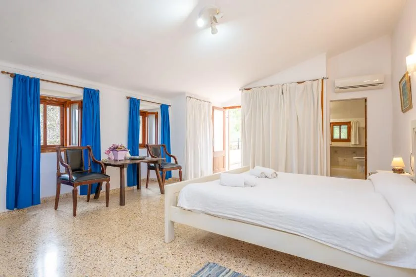 A bright bedroom with a large bed, blue curtains, and a small seating area.