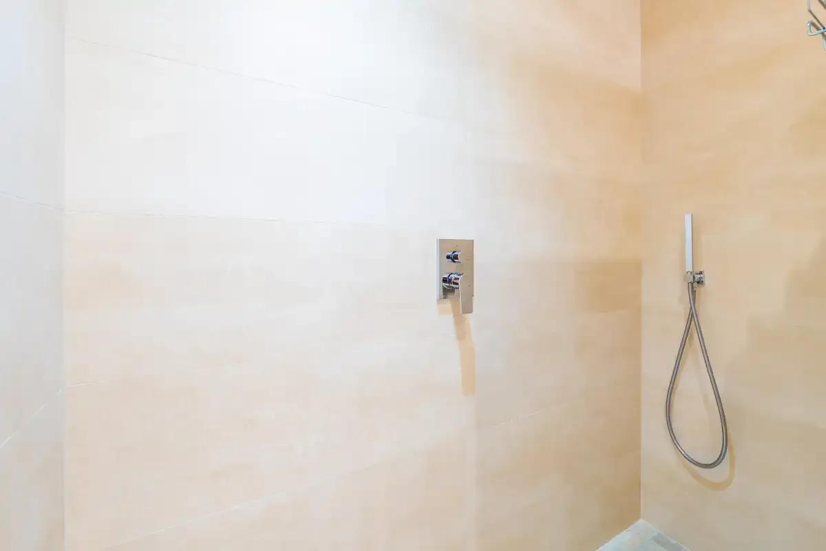 A tiled shower area with a wall-mounted control and handheld showerhead.
