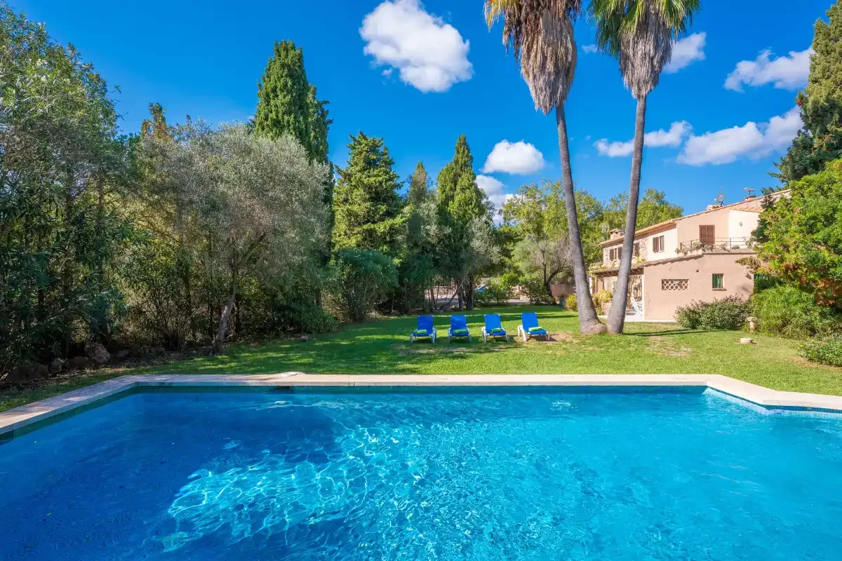 A swimming pool overlooks a garden with blue loungers and a house.