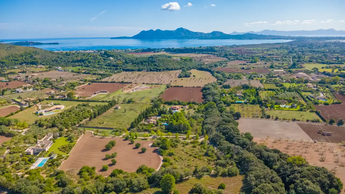 Aerial landscape of fields, scattered homes, and the sea in the distance.