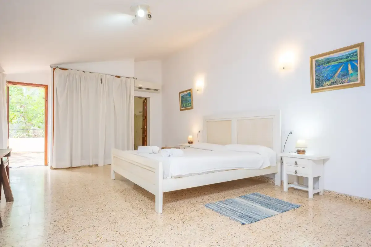 A bright bedroom with a white bed and curtains beside an open doorway.