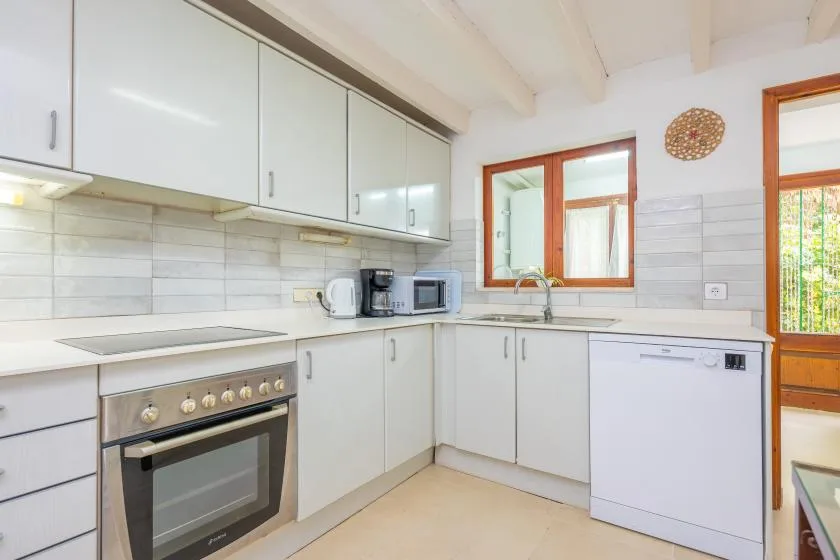 A bright kitchen with white cabinets, a cooktop, and a sink beneath the window.