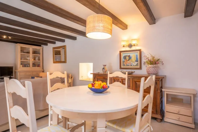 A bright dining room has a round table beneath exposed ceiling beams.