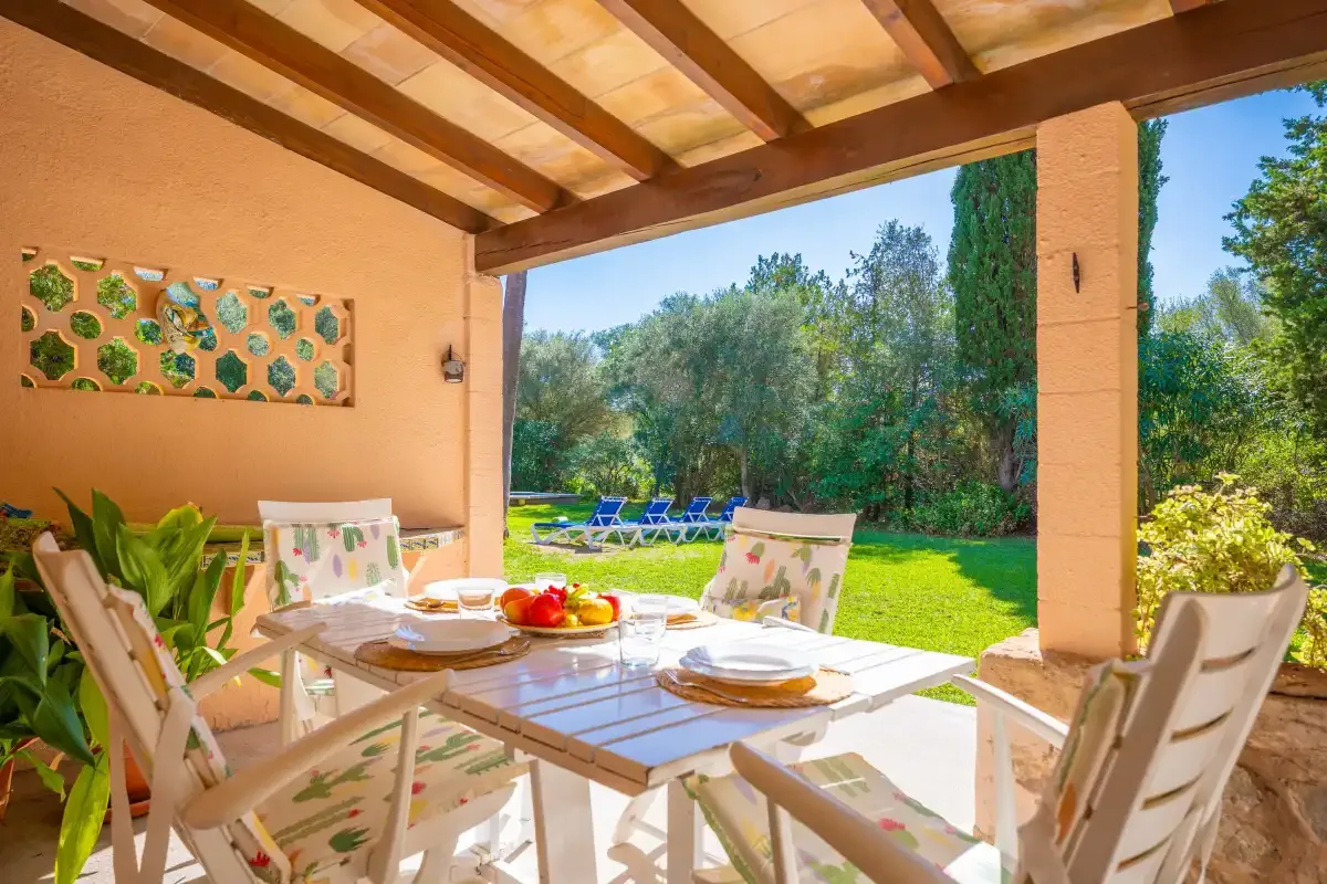 A covered outdoor dining area opens onto a garden with loungers.