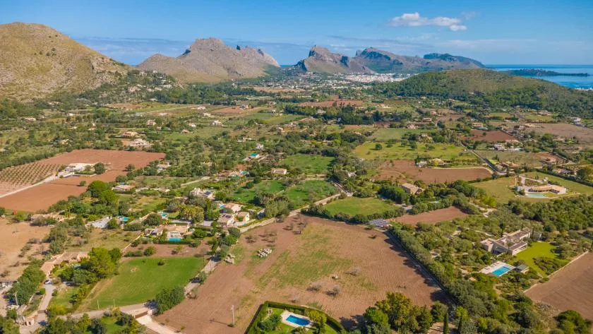 An aerial view of green fields and scattered homes beneath a mountain range.