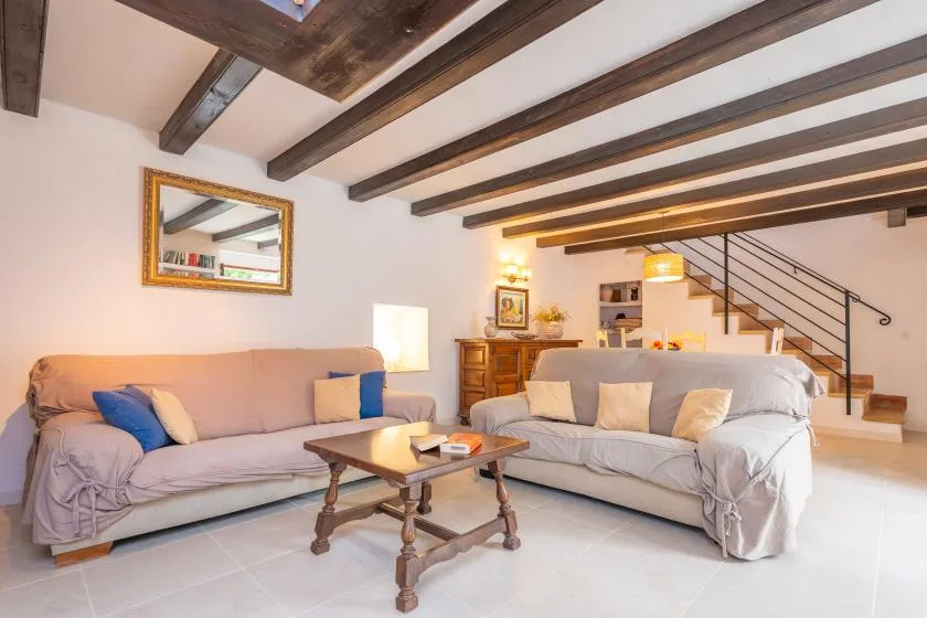 A living room with seating around a wooden coffee table beneath exposed ceiling beams.
