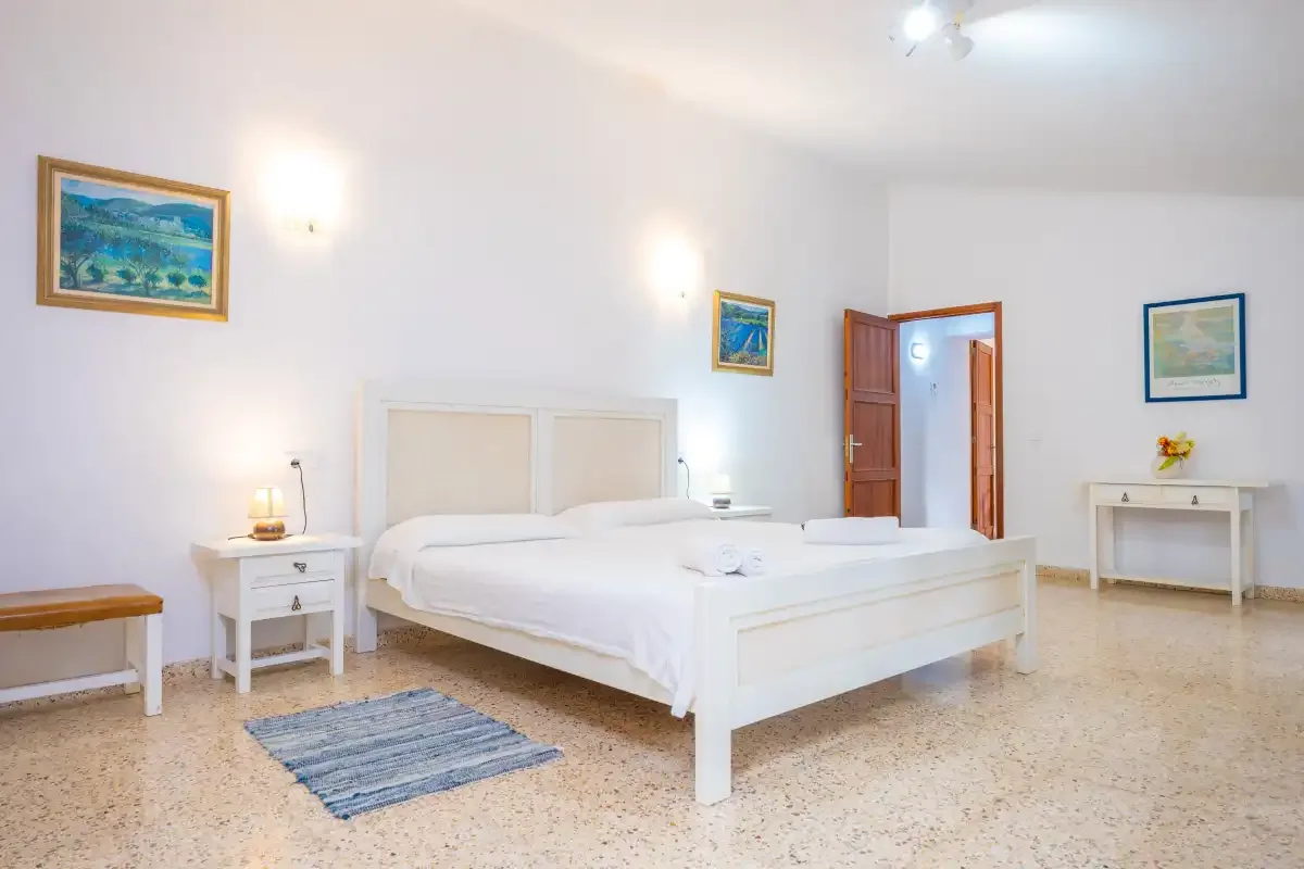 A bright bedroom with a white bed and framed landscape paintings.