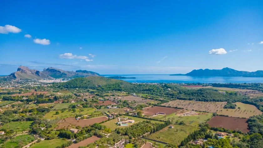 A wide rural landscape with fields, scattered homes, and a blue bay beneath a clear sky.