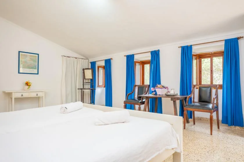 A bedroom with a large bed, blue curtains, and a table by the windows.