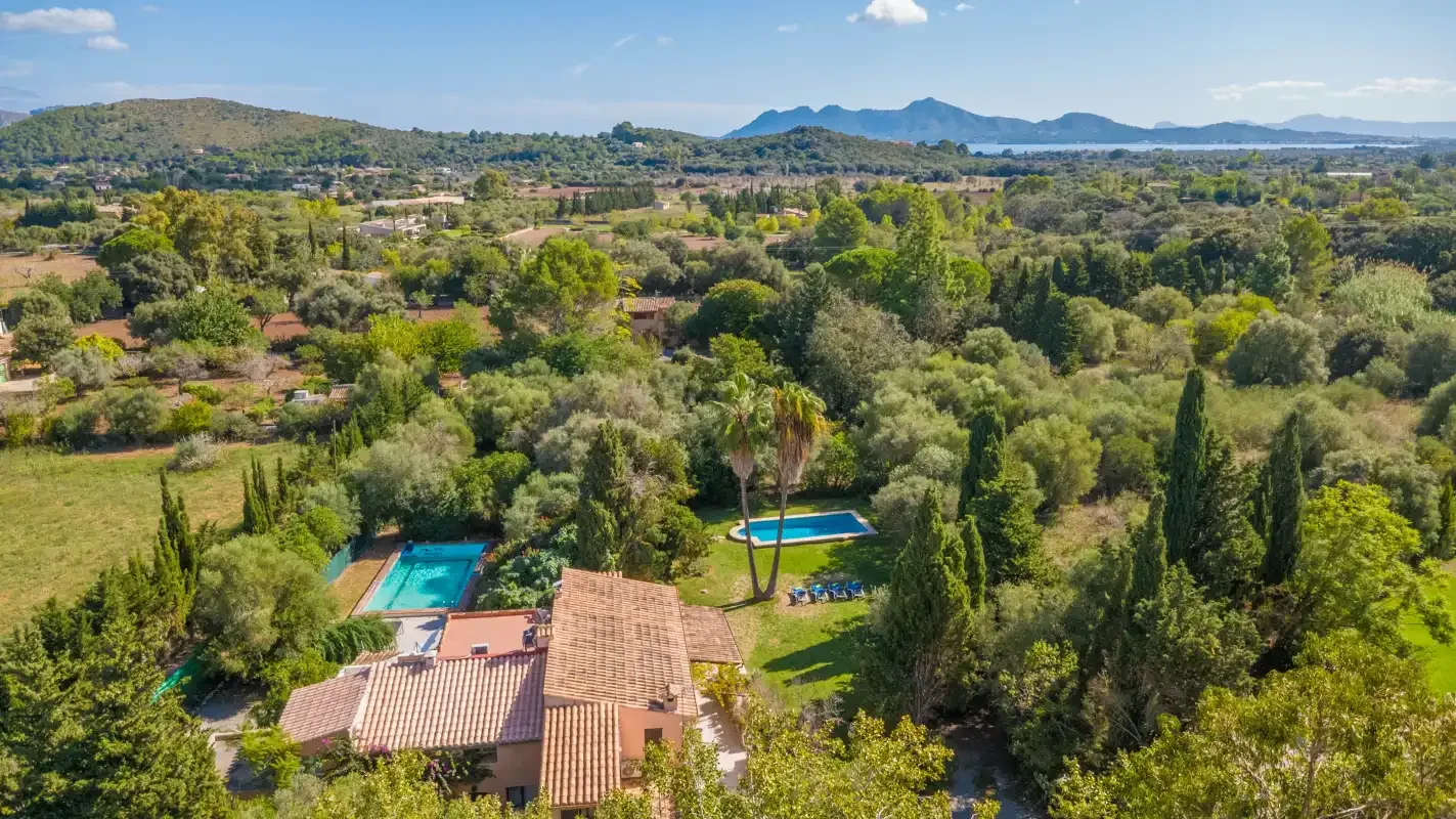 An aerial view of a terracotta-roofed house, swimming pool, and surrounding green landscape.