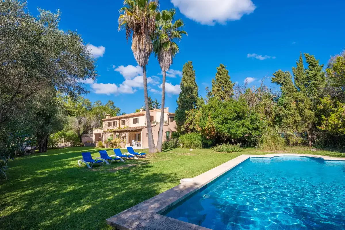 A garden and swimming pool beside a house, with lounge seating on the lawn.