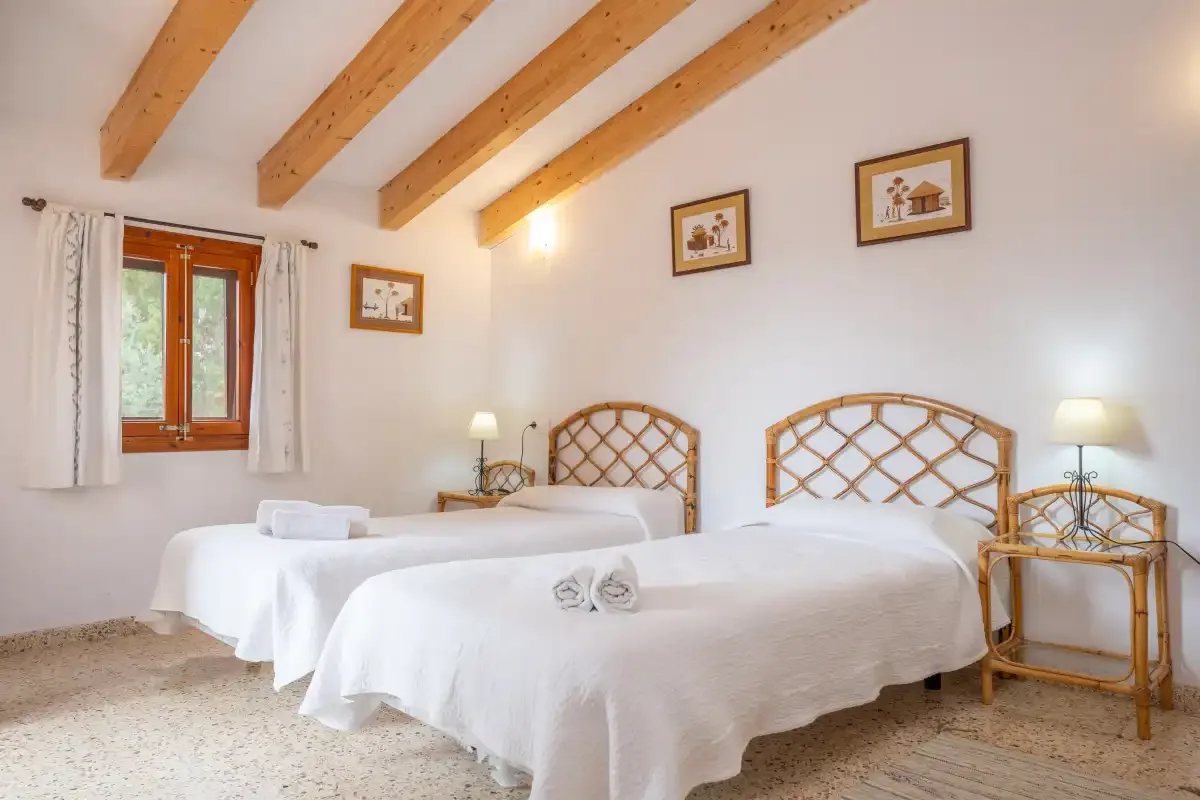 A bright bedroom with two beds, exposed wooden ceiling beams, and a window.