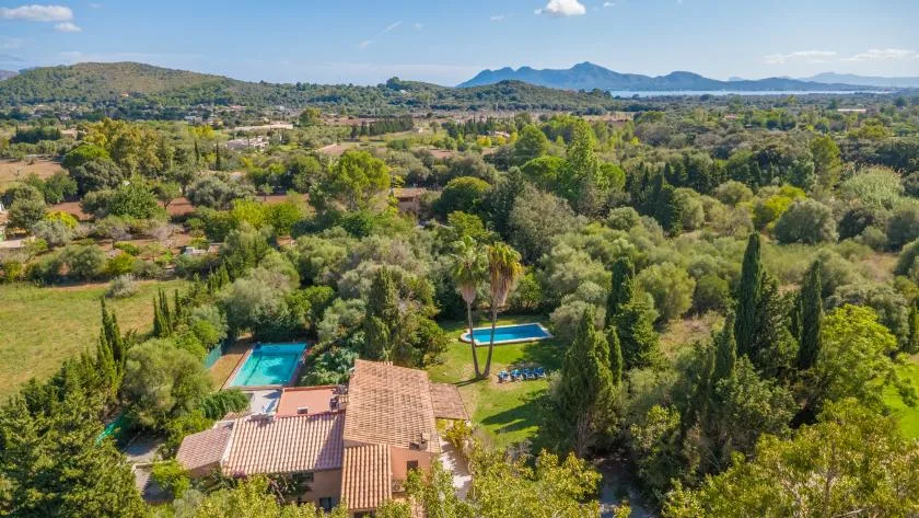 Aerial view of a house and swimming pools amid green countryside.