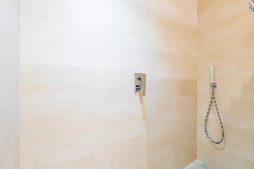 A tiled shower area with a wall-mounted control and handheld showerhead.