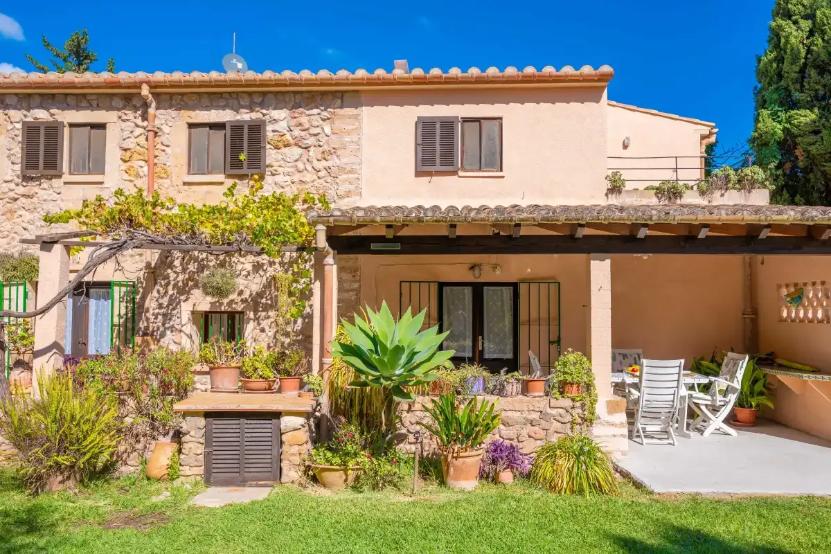 A stone and stucco house with a covered patio and garden plants.