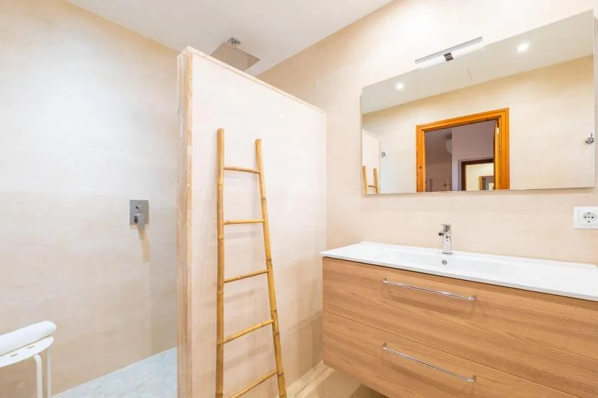 A bathroom vanity with a wide mirror and a wooden ladder leaning against the wall.
