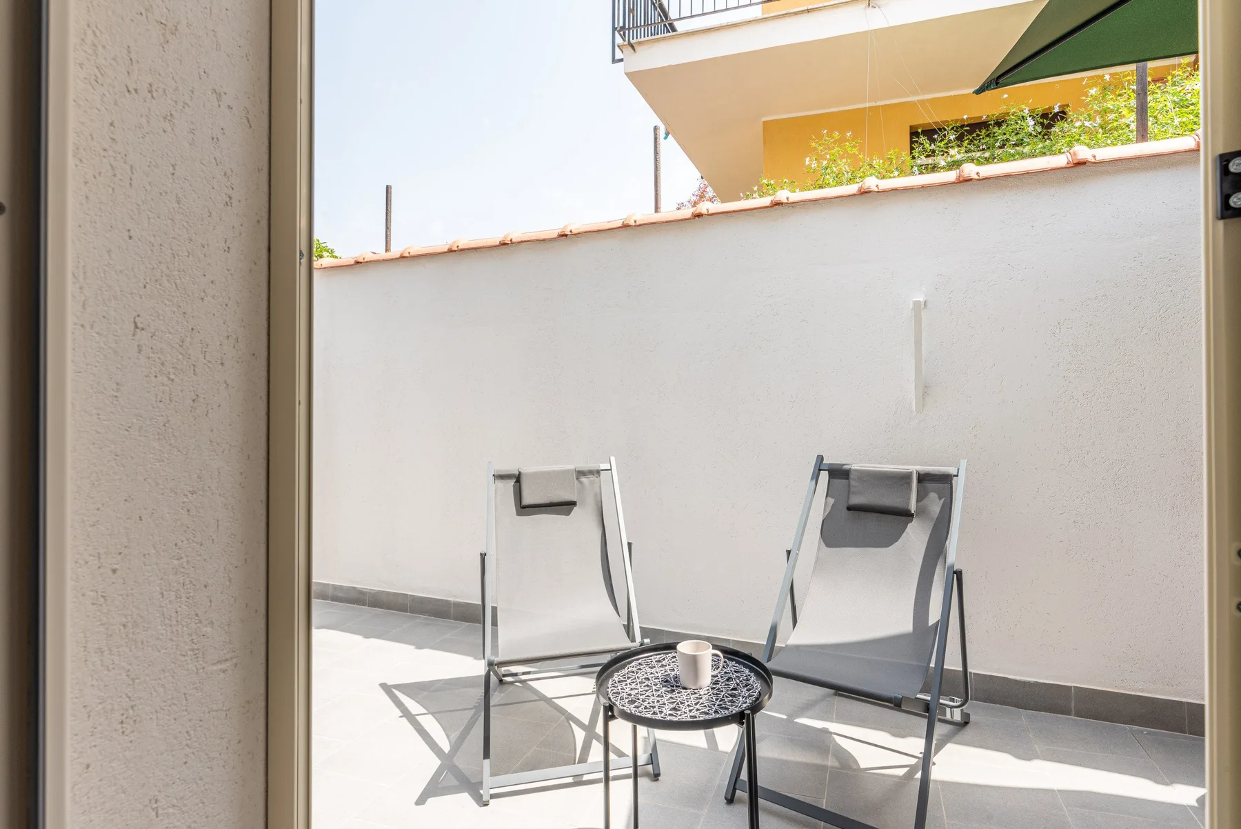 Un patio al aire libre con dos asientos y una mesa pequeña redonda.