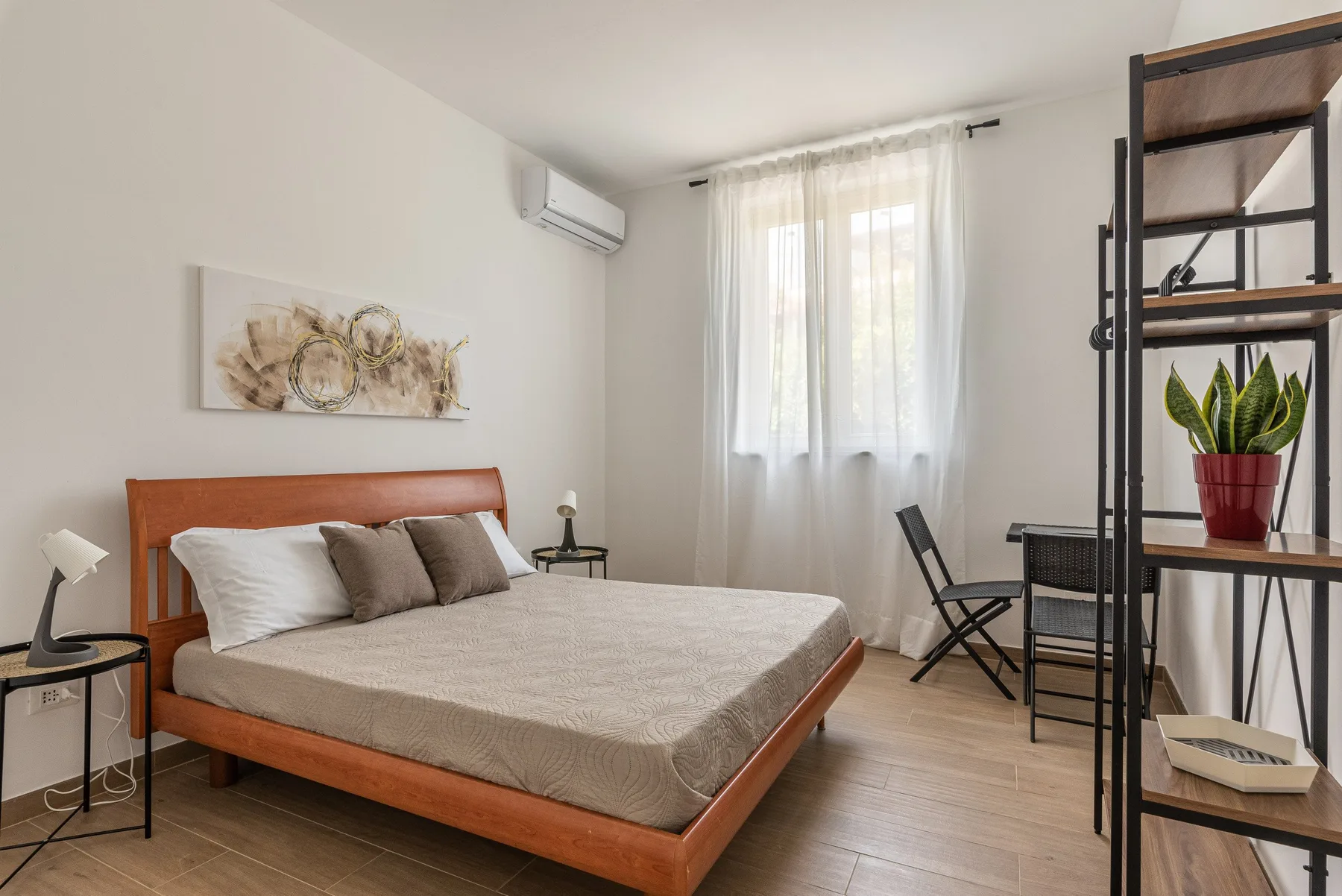 Un dormitorio luminoso con cama de madera, ropa de cama clara y cortinas translúcidas.