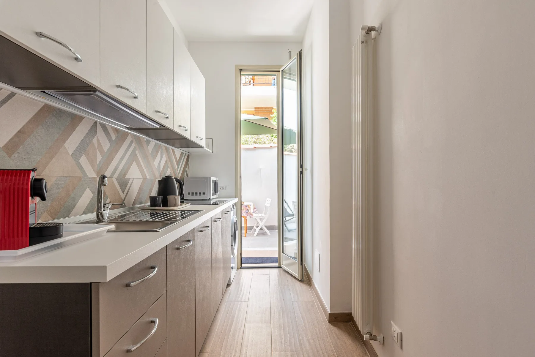 Una cocina estrecha con armarios y encimera conduce a una puerta de vidrio abierta.