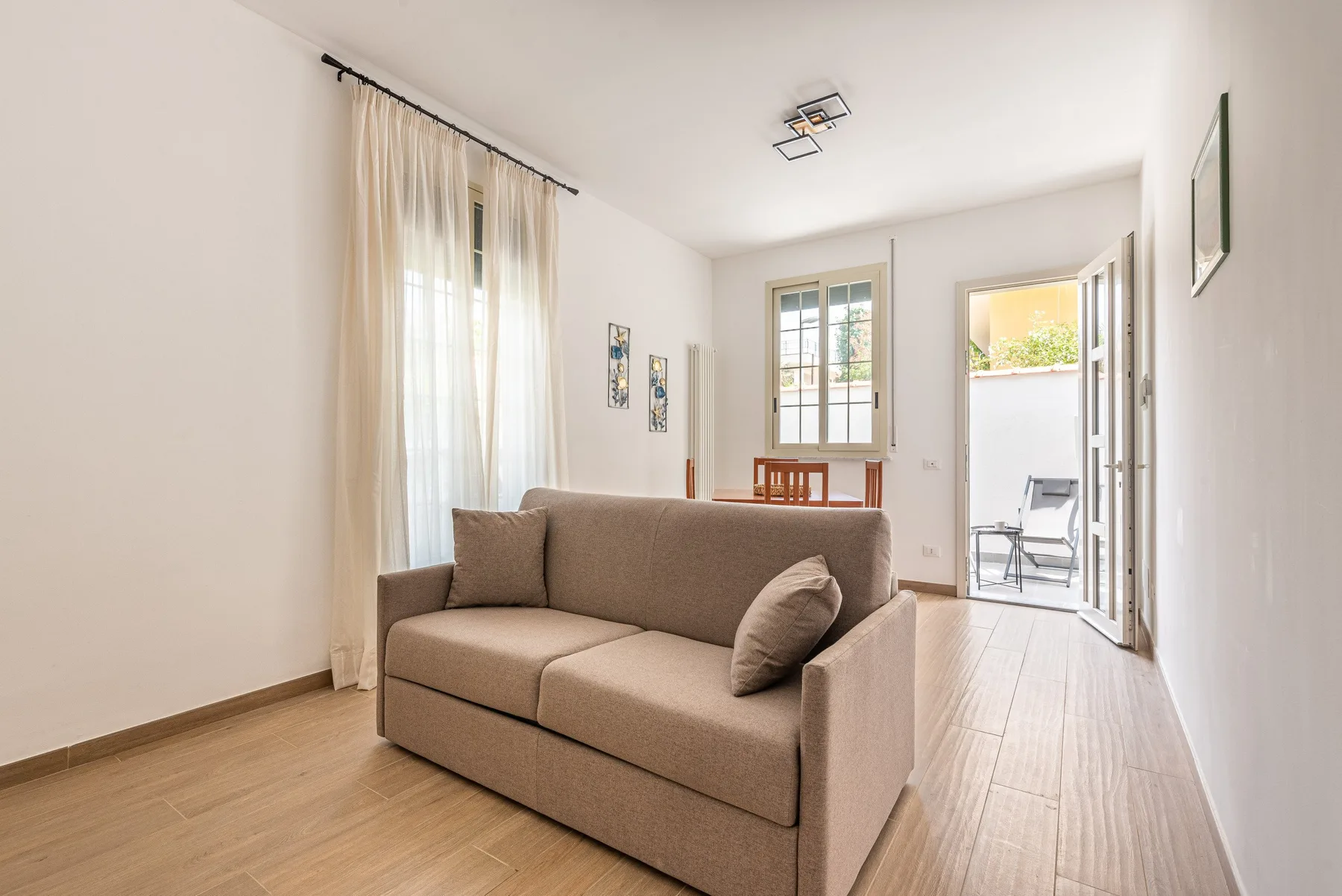 Una sala luminosa con un sofá beige y ventanas altas con cortinas.