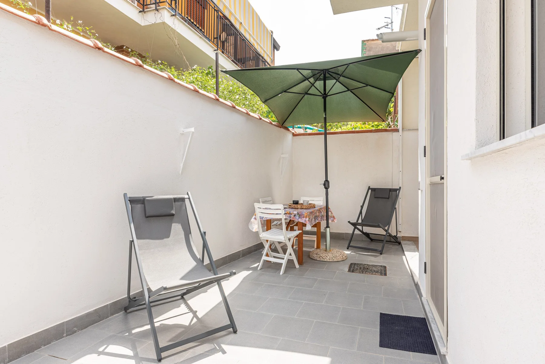 Un pequeño patio exterior tiene asientos y una sombrilla verde.