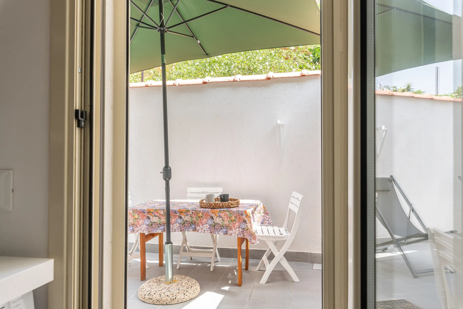 Una pequeña zona de comedor en el patio, con mesa y sillas bajo una sombrilla verde.