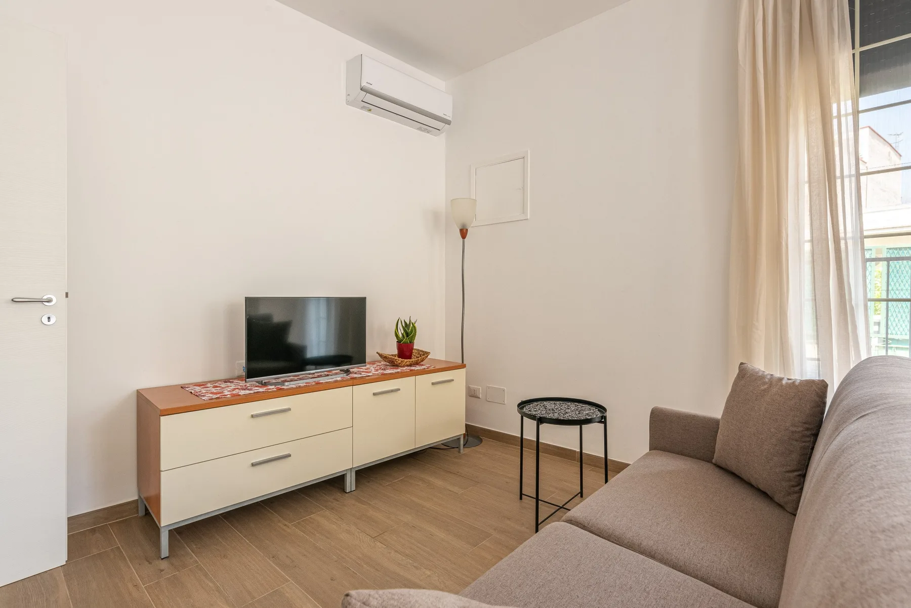 Una sala luminosa con un televisor sobre un mueble bajo y asientos junto a la ventana.
