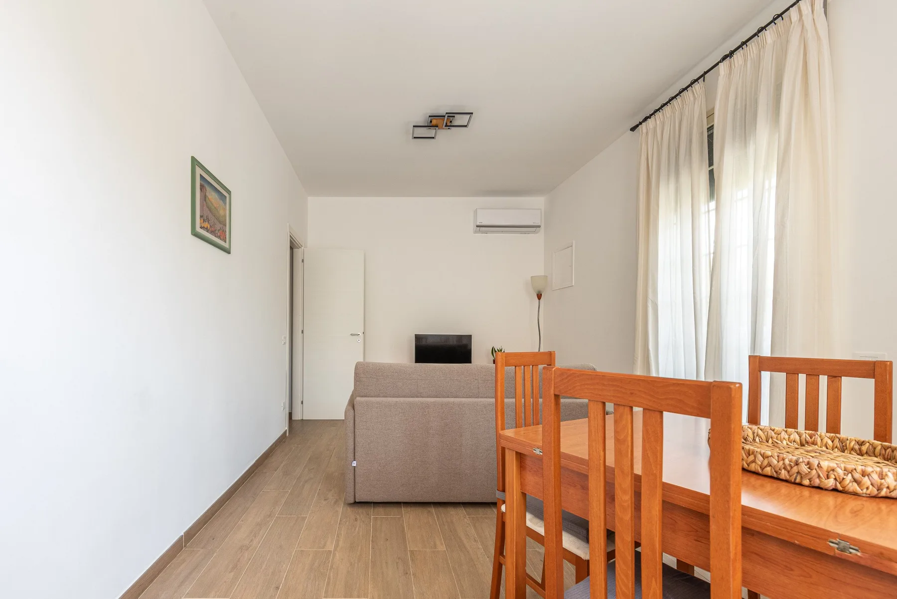 Una zona de estar y comedor con asientos de madera y grandes ventanas con cortinas.