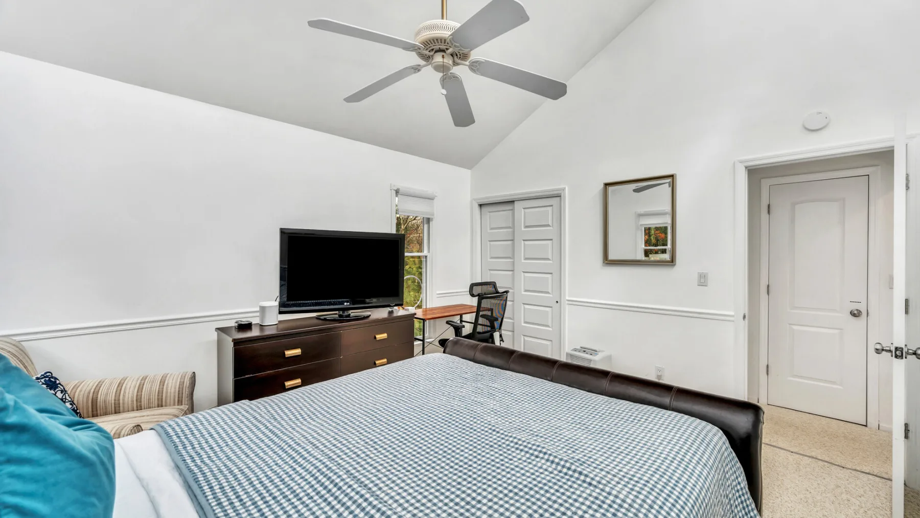 Un dormitorio con una cama bien tendida, una cómoda y un ventilador de techo.