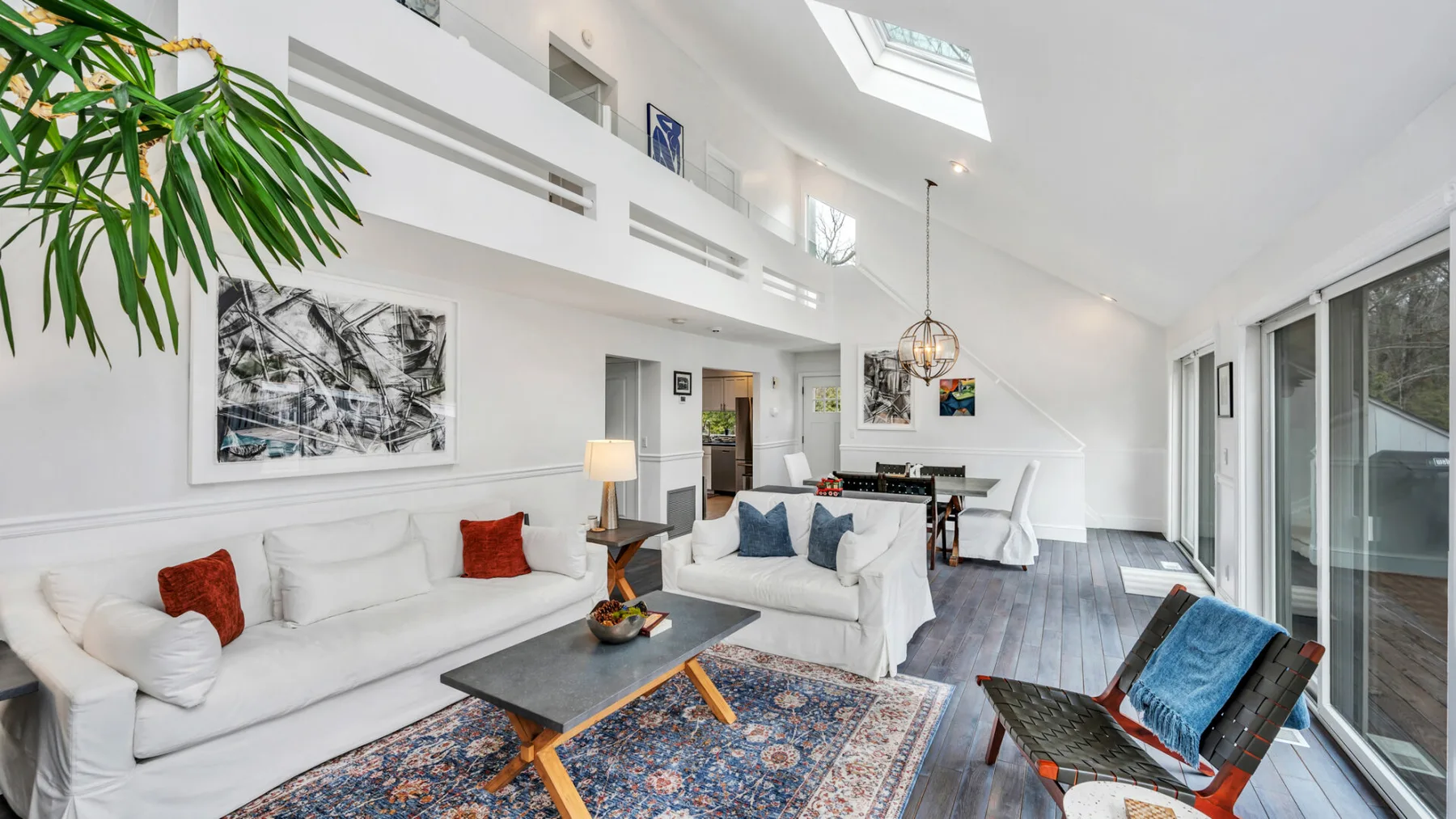 Una sala luminosa con asientos blancos, una alfombra estampada y un techo alto.